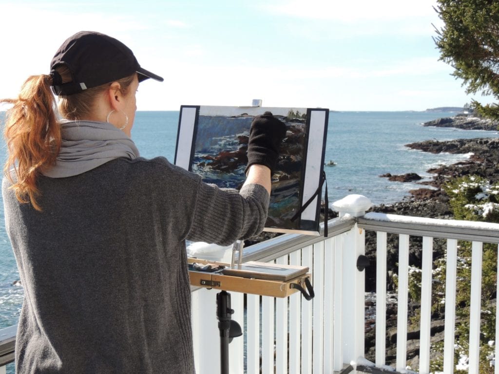 Lyn at her easel, on a rugged coastline.