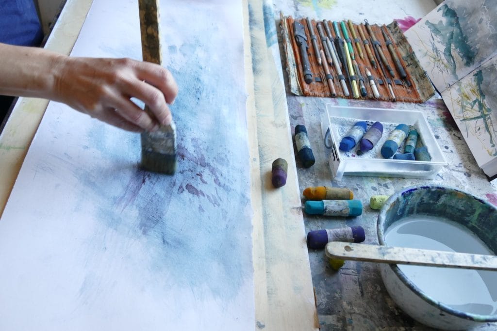 Libby works the wet pastel into the paper with a paintbrush.