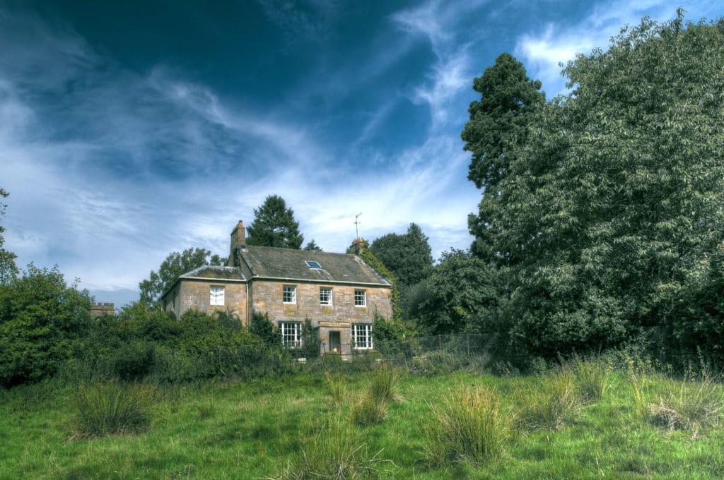 The Old Rectory set amongst fields and woodland, with a dramatic blue sky with wispy clouds.