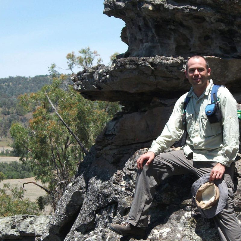 A photo of Brent sitting on a rock, in the Australian outdoors.