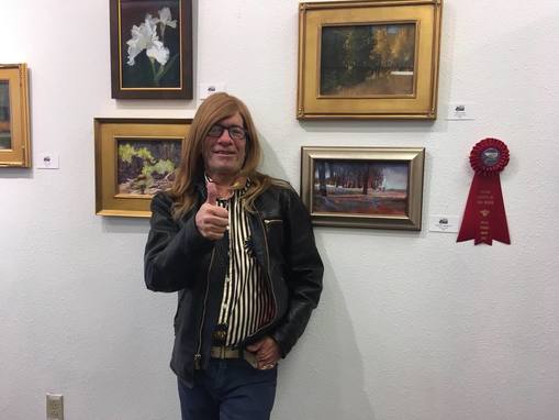 RS Weinblatt giving a thumbs up to the camera, while standing infront of a gallery of his work.