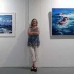 Tricia Taylor poses between two of her seascape pieces at her exhibition.