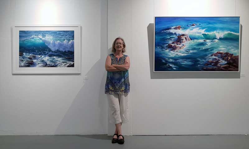 Tricia Taylor poses between two of her seascape pieces at her exhibition.