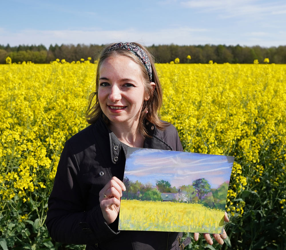 Cindy holding her painting in a rapeseed field.