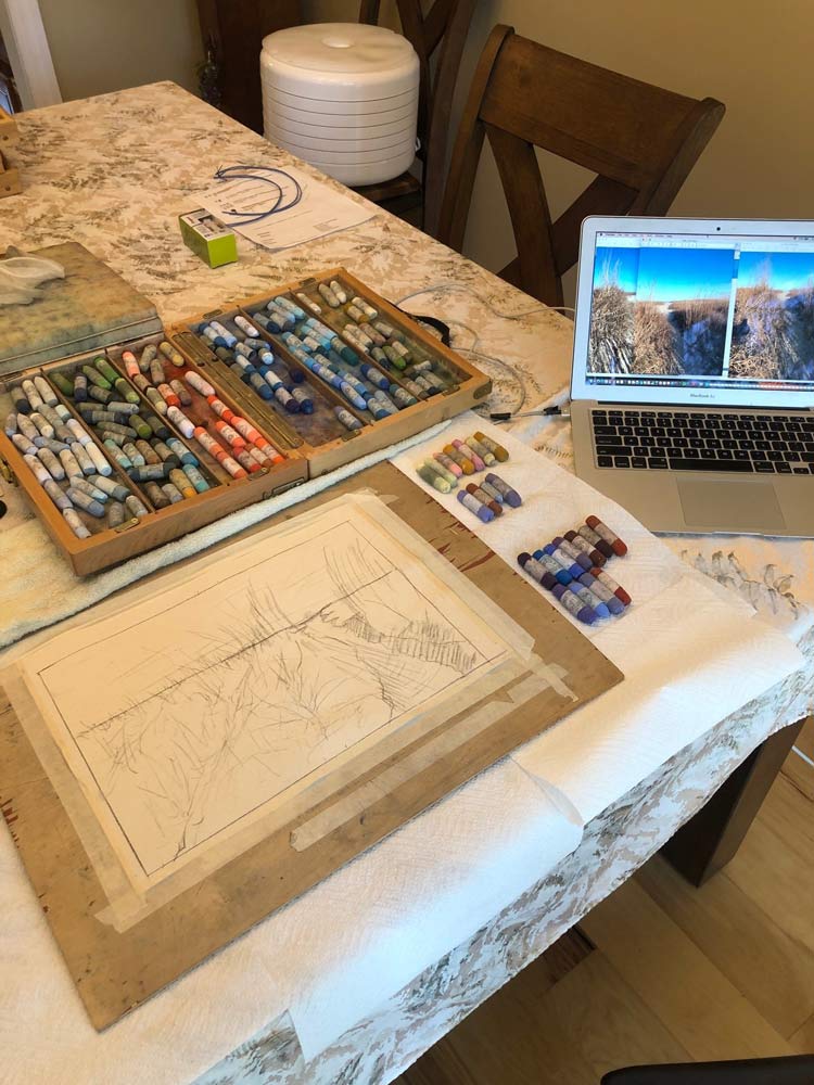Worktable with pastels and painting, with laptop showing reference image.