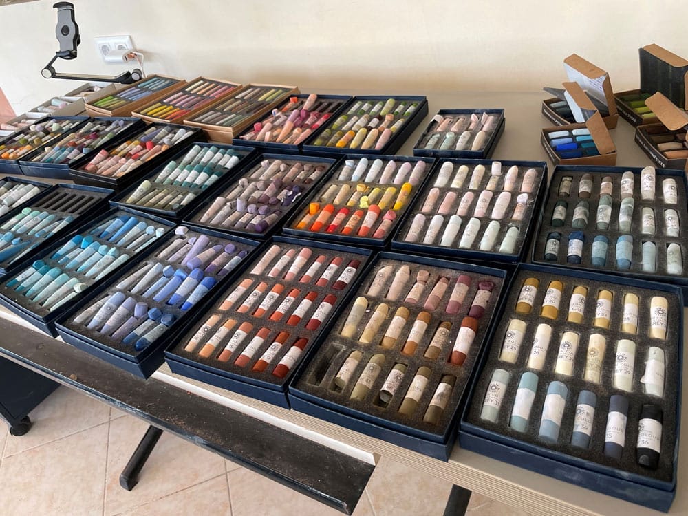 Lots of coloured pastel sets laid out on a table.
