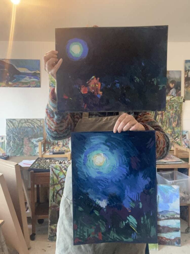 Amy hold's a couple of her paintings up for the camera.