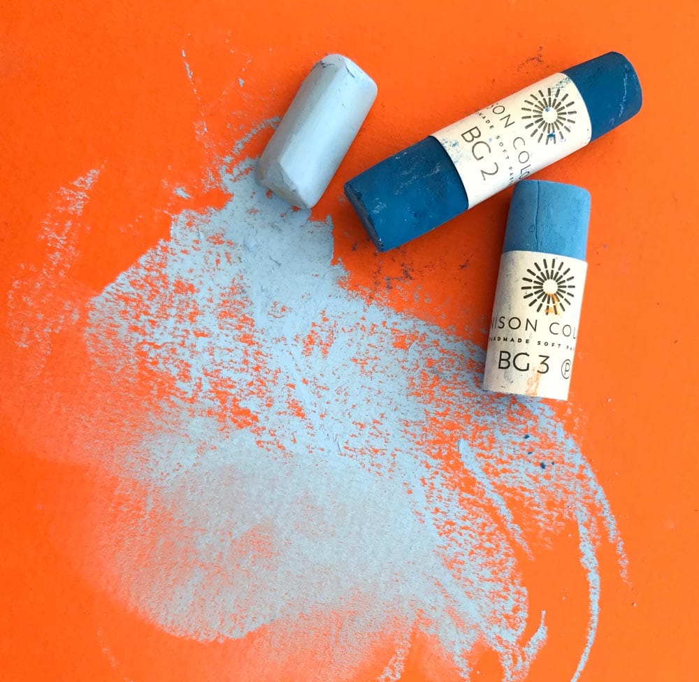 Well used pastels laying on an piece or orange pastel card.