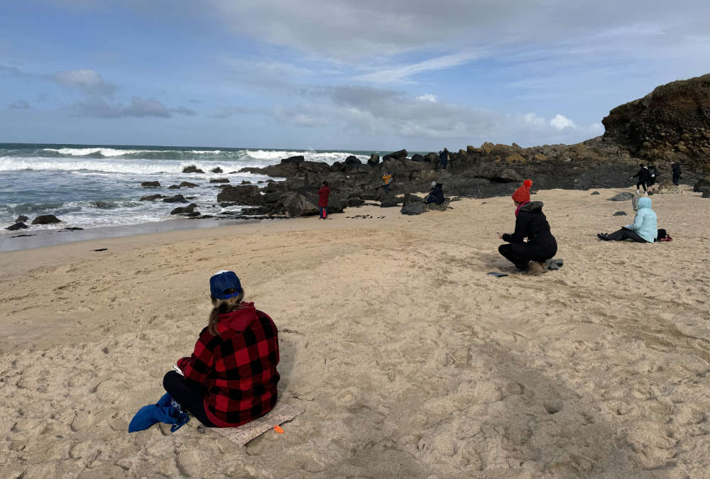 Student artists paint on the beach.