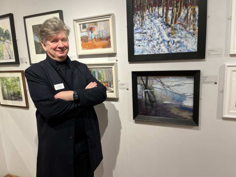 Arild Frisnes standing next to his paintings at the exhibition.